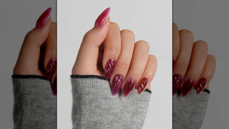 Main fermée montrant une manucure couleur baie avec une texture 3D