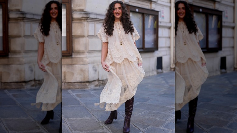 Une femme vêtue d'une jupe midi blanche avec de hautes bottes en cuir foncé