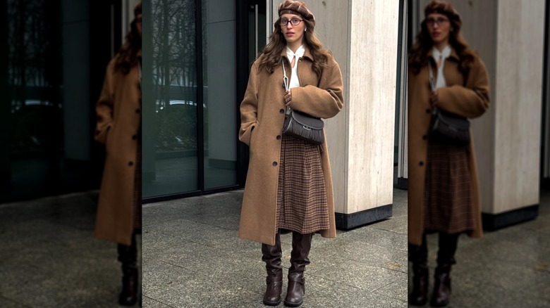 Une femme portant un béret et un manteau marron avec une jupe et des bottes à l'extérieur