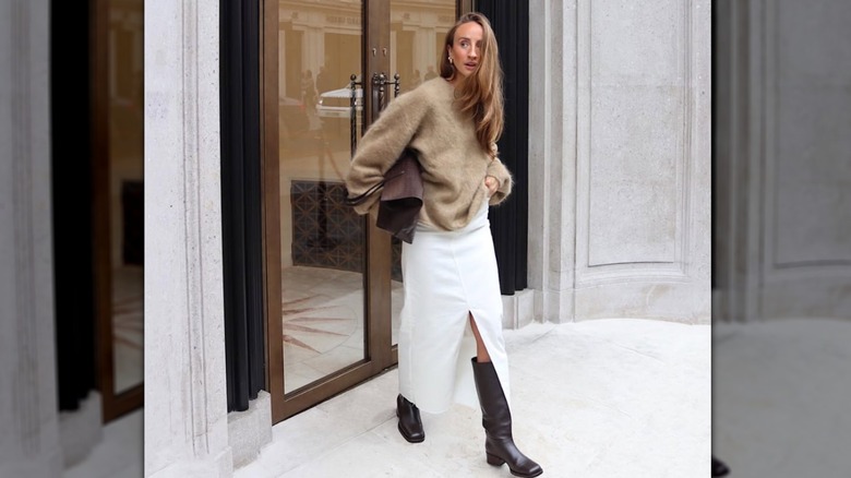 Une femme avec une jupe blanche avec une fente sur le devant et des bottes marron marchant dehors