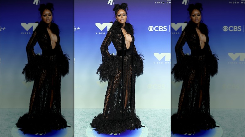 Teyana Taylor debout avec sa main sur ses hanches tout en portant une robe manteau décolletée