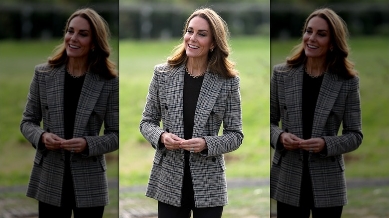 Kate Middleton debout dans un champ portant un blazer à carreaux
