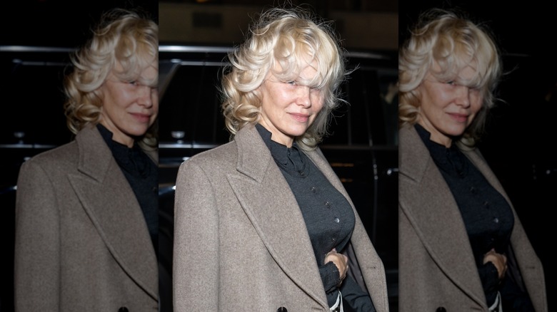 Pamela Anderson portant une chemise noire et un blazer marron avec des cheveux courts