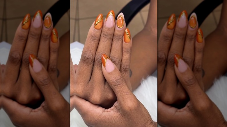 Deux mains montrant un ensemble d'ongles avec un œil de chat orange et des accents dorés