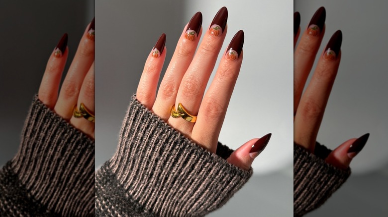Main ouverte montrant une manucure française en demi-lune avec une citrouille peinte à la main à la base de chaque ongle