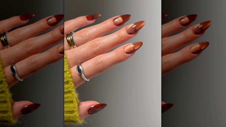 Main ouverte montrant les ongles avec un vernis à ongles orange brunâtre et un effet œil de chat
