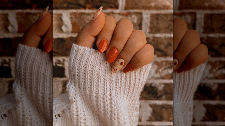Main fermée montrant un ensemble de clous avec des clous orange uni et deux clous décoratifs beiges avec des feuilles d'automne