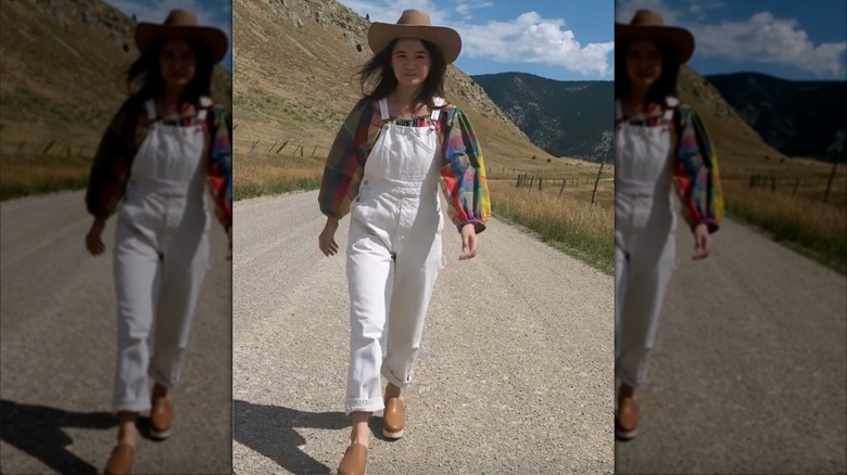 Une femme en salopette blanche avec une chemise brillante et un chapeau de cowboy en marchant dehors