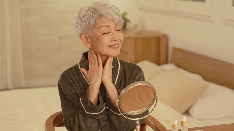 Femme plus âgée regardant dans un miroir hydratant la peau
