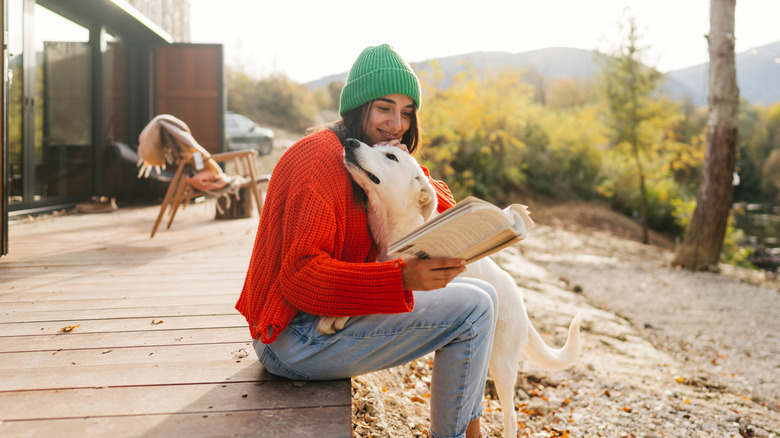 Une jeune femme caressant son chien tout en lisant un livre et en profitant de son après-midi dehors
