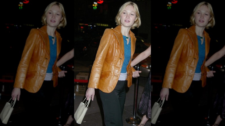 Julia Stiles porte un pantalon noir, un haut turquoise et une veste en cuir marron caramel