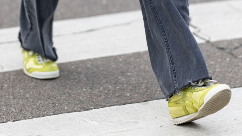 Les pieds d'une femme marchant dans des baskets jaunes tout en portant un jean foncé