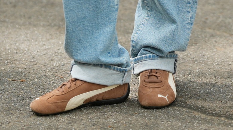 Les pieds d'une femme portant des baskets fines marron avec un jean bleu retroussé