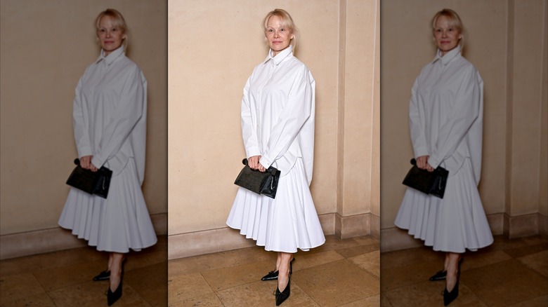 Pamela Anderson portant une jupe plissée blanche et une chemise blanche lors d'un événement