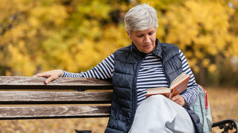 Femme âgée se détendant sur un banc de parc, lisant un livre en automne