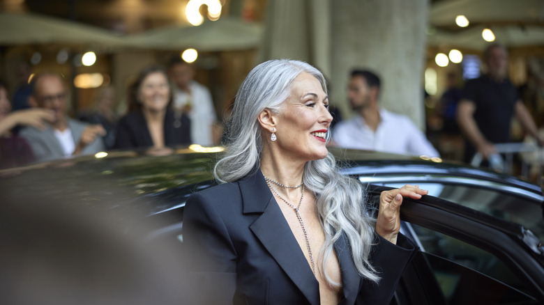 Une femme aux cheveux gris sort de sa voiture et pose pour des photos