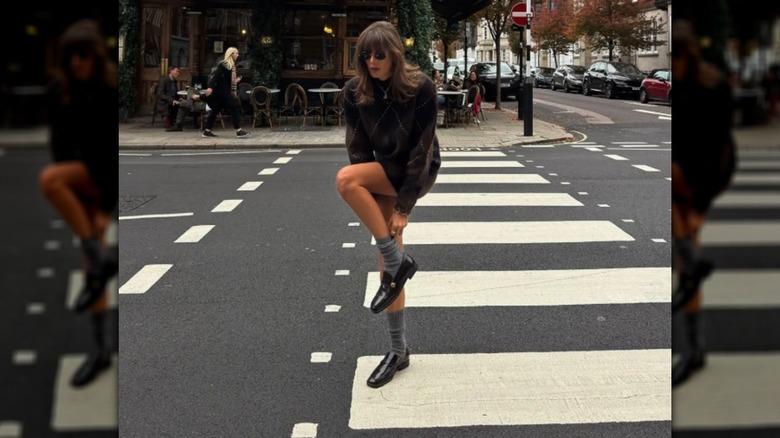 Julie Sergent Ferreri remonte ses chaussettes grises portant une veste marron et des mocassins noirs