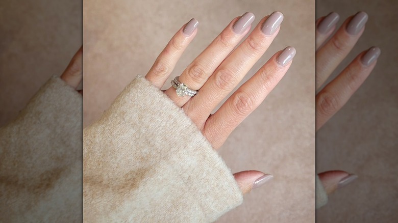 Une main ouverte portant une bague scintillante et une manche crème et montrant la teinte neutre Lowkey Perfect d'Olive & June