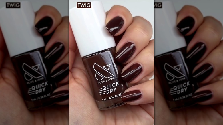Gros plan de quatre clous contre une bouteille de vernis à ongles Olive & June montrant la teinte marron Twig