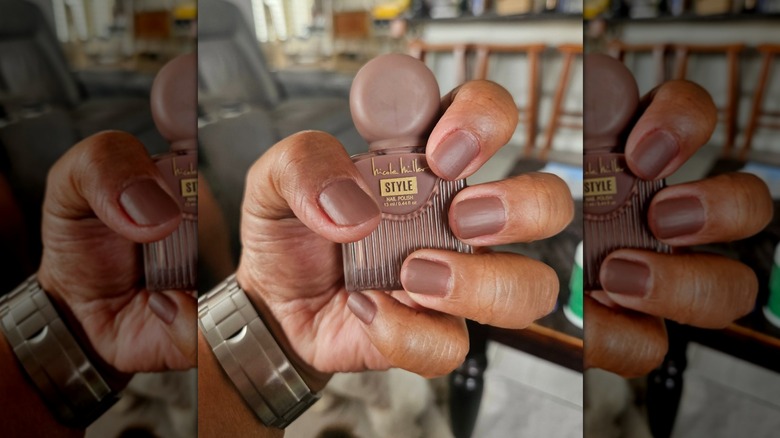 Une main tenant une bouteille de vernis à ongles Nicole Miller tout en montrant la teinte marron clair correspondante