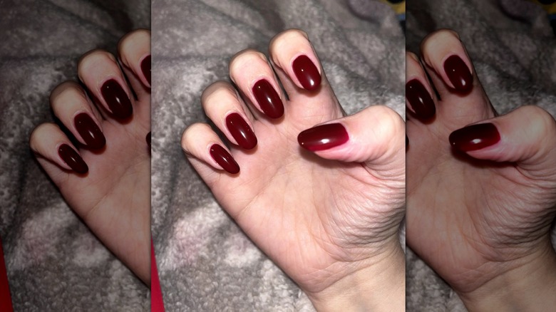 Une main semi-fermée exhibant un vernis à ongles rouge foncé avec une couverture grise en arrière-plan