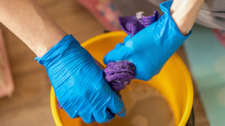 Femme portant des gants en latex bleu et essorant un chiffon violet