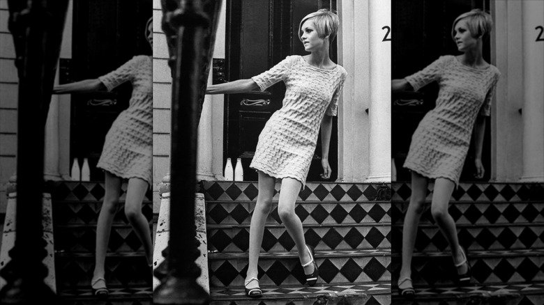 Twiggy s'accroche à une rampe et porte une mini-robe blanche.