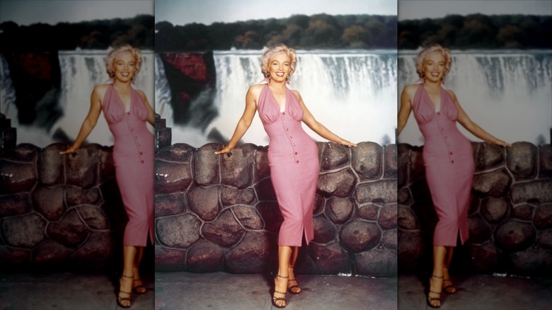 Marilyn Monroe porte une robe boutonnée rose et des talons à lanières.