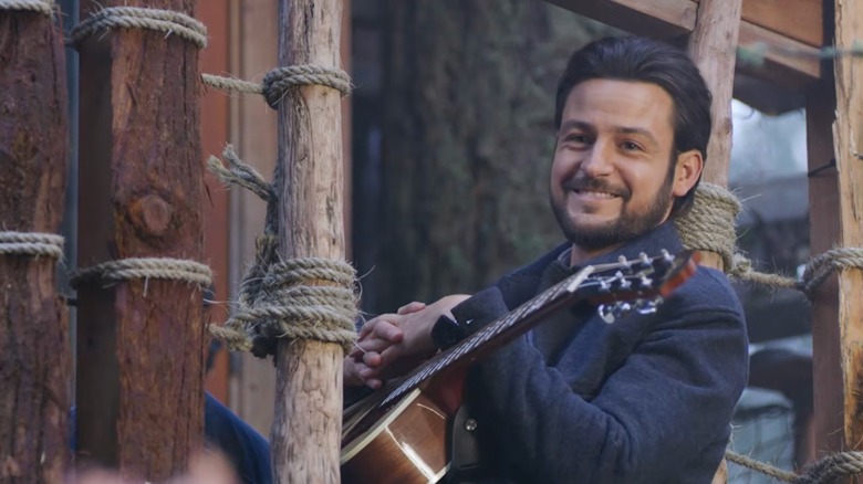 Tyler Hynes joue de la guitare dehors, sur un porche en bois. 