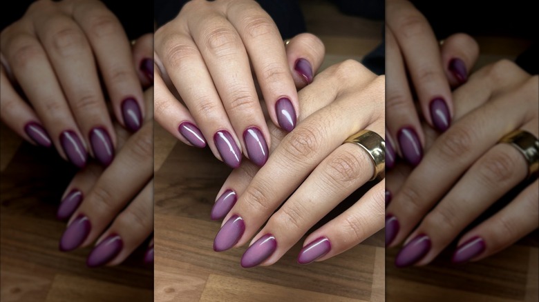 Mains posées sur une table avec une manucure violette aura