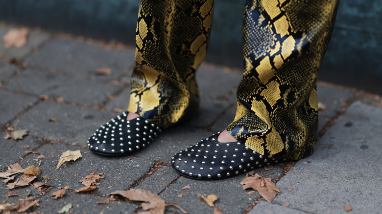 Personne portant des ballerines cloutées et un pantalon en peau de serpent