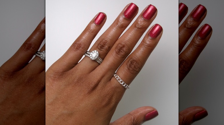 Main ouverte montrant des ongles rouge cerise avec un soupçon d'éclat sur un fond blanc