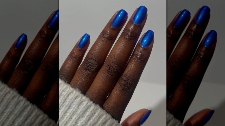 Main ouverte montrant des ongles bleu vif avec un léger éclat sur fond gris
