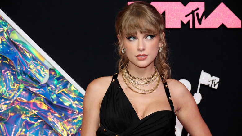 Taylor Swift regardant sur le côté tout en portant une robe noire et des colliers superposés aux MTV VMA 2023