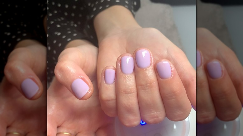 Une femme montrant une manucure lavande laiteuse sur des ongles courts