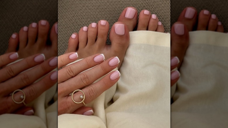Une femme avec une pédicure rose et une manucure à pointe française vêtue de blanc