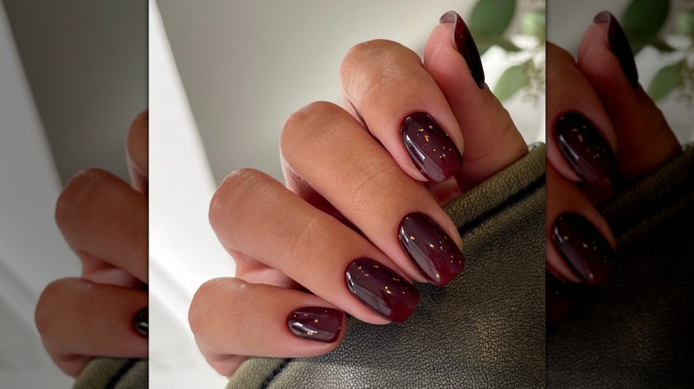 L'artiste des ongles montre sa manucure bordeaux.