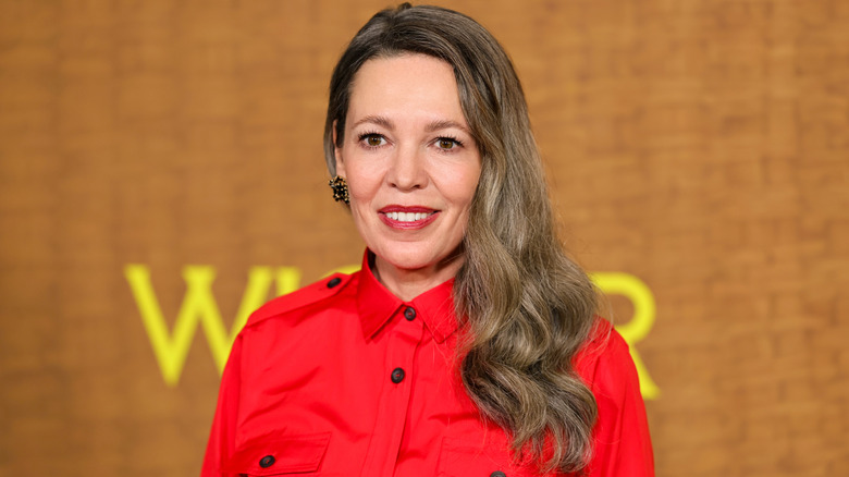 Olivia Colman sur le tapis rouge avec une chemise rouge et de longs cheveux gris