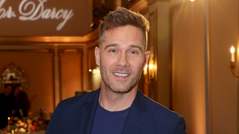 Luke Macfarlane souriant à la caméra dans une salle de bal